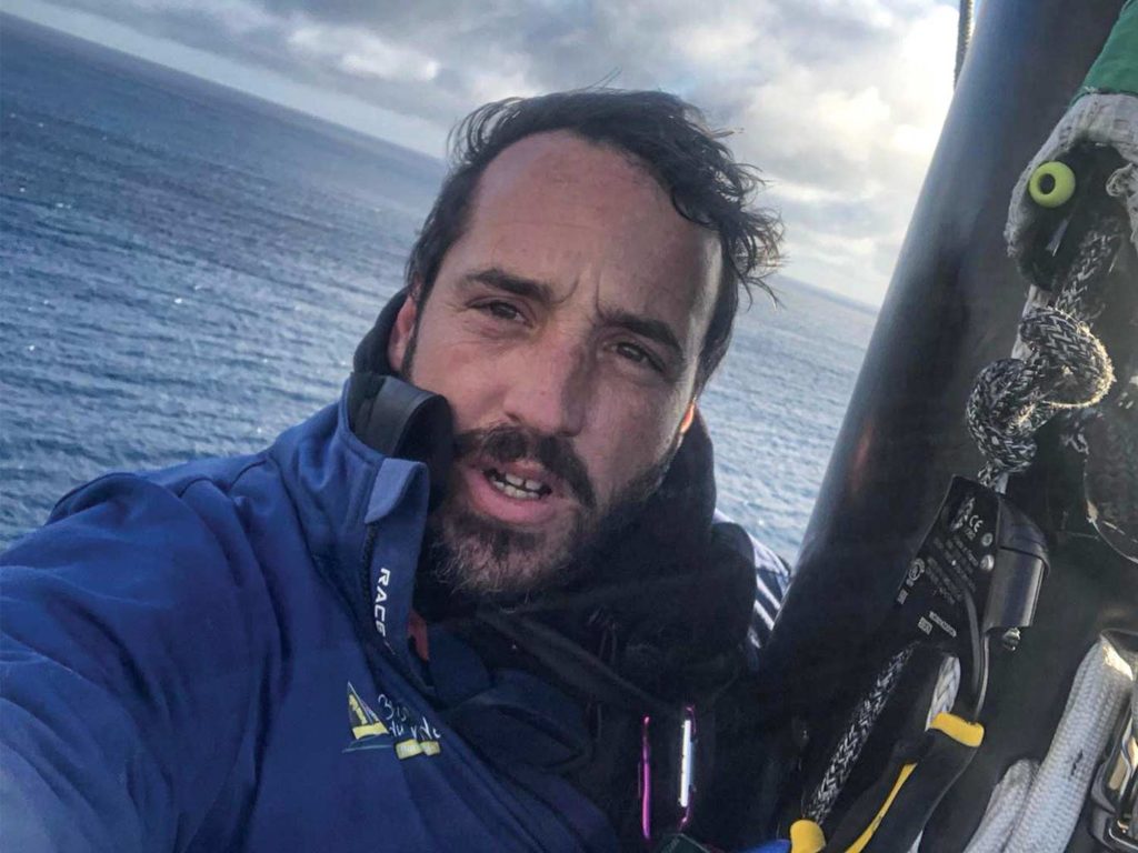 A sailboat racer takes a selfie atop his boat.