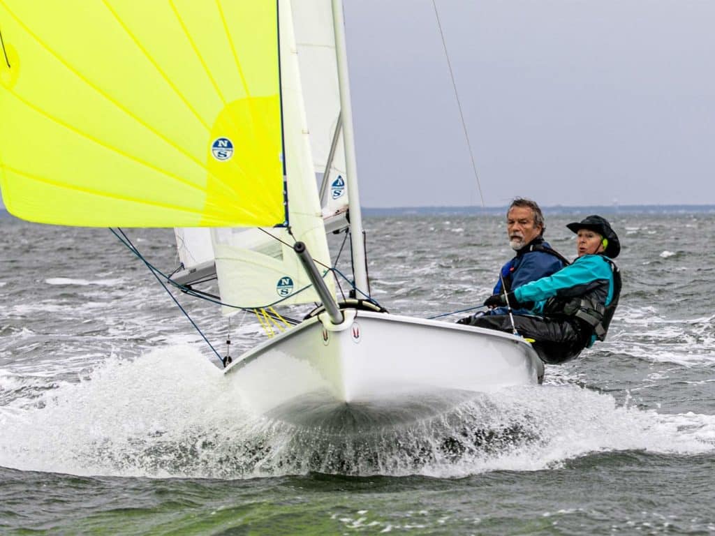 Two people pilot a sailboat across the water.